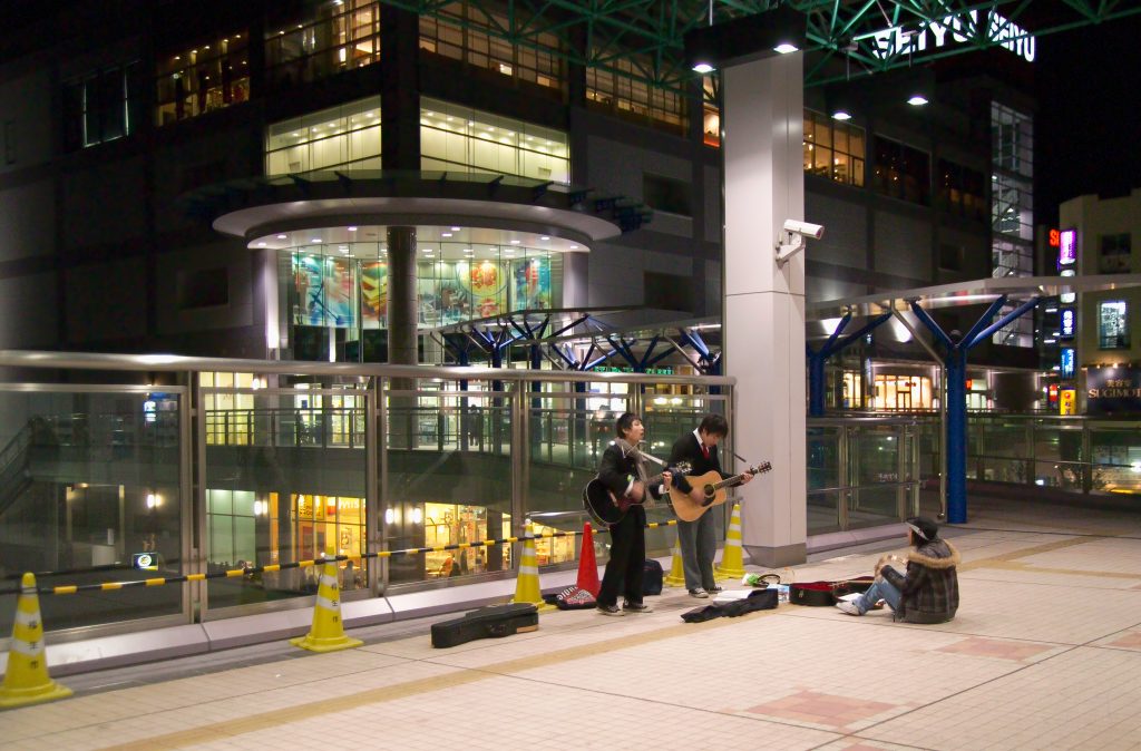 two guys playing guitar in front of seiyu in fussa japan